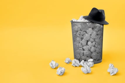 Black hat sitting on full waste basket with a yellow background